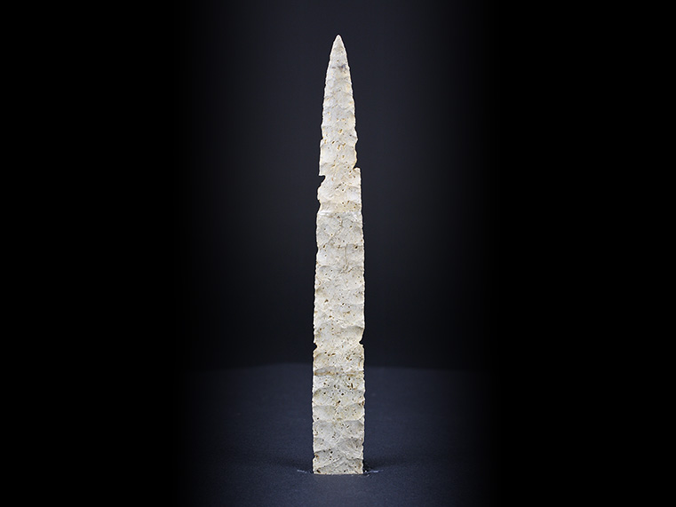 Ochre-coloured chipped stone. It is lance-shaped, long and narrow. It has a straight base. Arrows enable it to be turned.