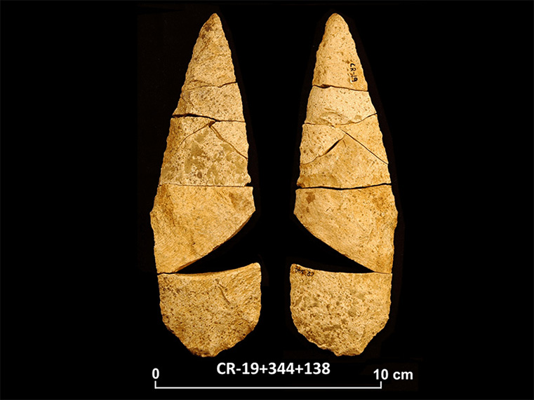Deux faces d’un assemblage de fragments de pierre taillée beige, créant une forme lancéolée.  Il manque un fragment triangulaire au-dessus de la base pour que la forme soit complète. Une longue cote et une échelle 0 à 10 centimètres sont inscrites en dessous.