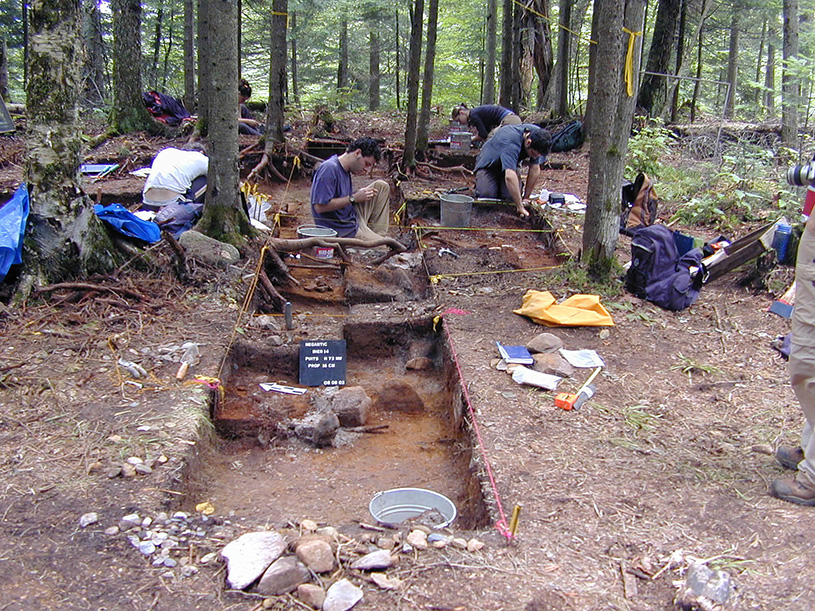 Bird’s-eye view of excavators and their equipment (bucket, gourd, tablet) inside an excavated square. Six people are in the photo.