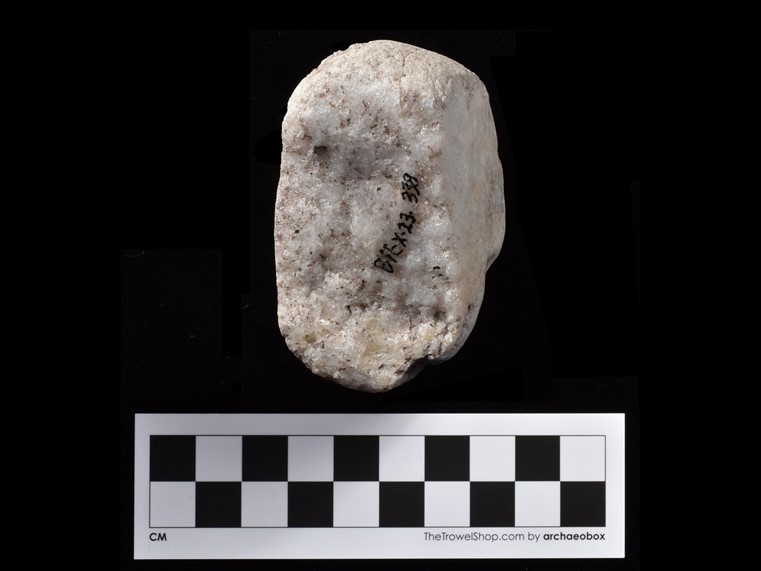 Block of white stone with a rounded top. The number BiEx-23.338 is inscribed on the stone in black. Below the image is a photographic scale in centimetres with black and white squares.