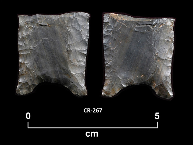 Two sides of a fragment of grey-green chipped stone. Both sides are slightly concave with thinned edges and a concave grooved base. The number CR-267 and a scale of 1 unit:5 cm are shown below.