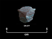 Chipped stone shard of a reddish and green colour with a small spur on each side and a pointed front. The number CR-377 and a scale of 1 unit:5 cm are shown below.