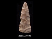White-ochre, oval lance-shaped chipped stone. There are visible marks of parts that were chipped off the edge of the point. The number BiEx-23.606 is inscribed on the bottom.