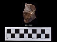 A block of reddish stone, more or less pyramidal, with a missing piece at its peak. The number BiEx-23.311 is inscribed on the bottom. Below the image is a photographic scale with black and white squares.